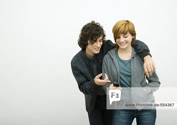 Young adult couple  man with arm around woman  woman holding cell phone