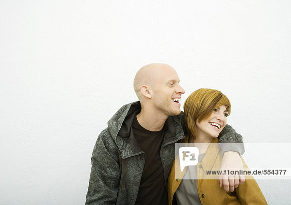Junges erwachsenes Paar  aus dem Rahmen schauend  lachend  Mann mit Arm um Frau herum