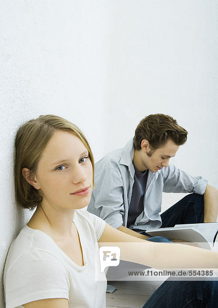 Teenage girl and young man sitting on floor  girl looking at camera