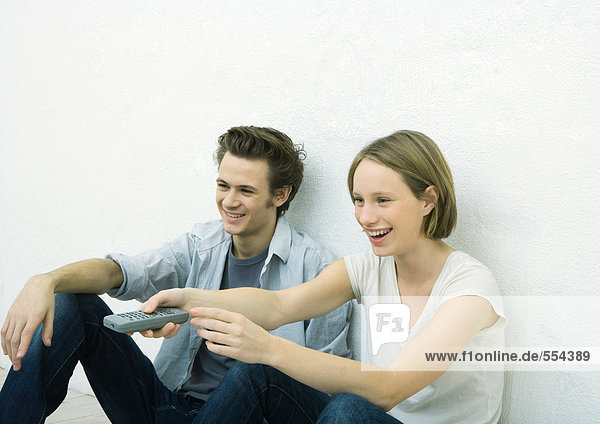 Teenage girl and young man sitting on floor  girl pointing remote control out of frame