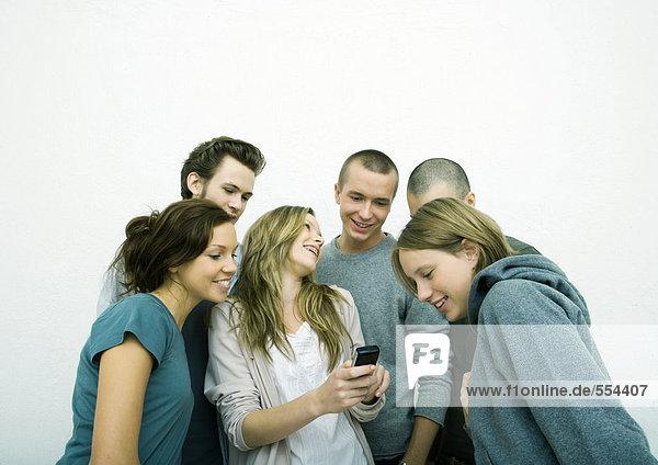 Group of young adult and teenage friends looking at cell phone  white background