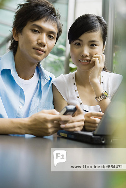 Junger Mann und Frau mit Laptop und Handy  Blick auf Kamera