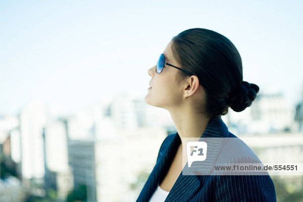 Woman wearing sunglasses  looking up  skyline in background  profile