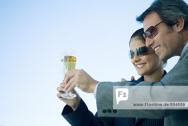 Mann und Frau klirren mit Champagner  Himmel im Hintergrund