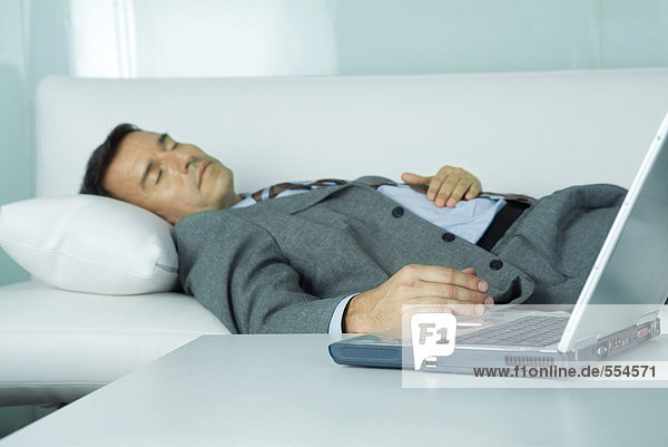 Geschäftsmann schläft auf Sofa  Hand ruht auf Laptop