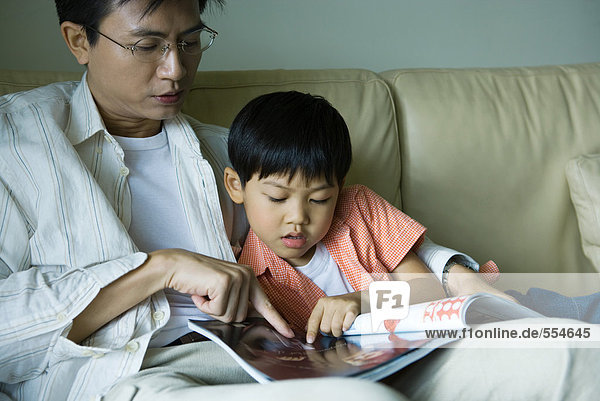 Vater und Sohn sitzen auf dem Sofa und schauen sich die Zeitschrift an.