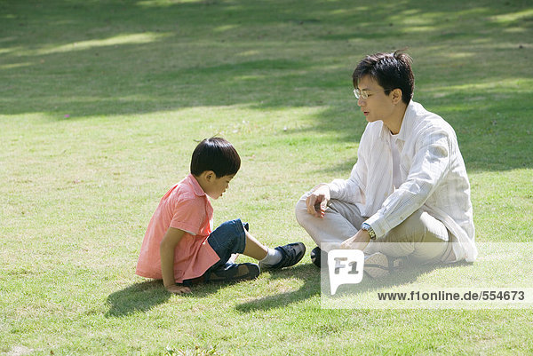 Vater und Sohn sitzen auf Rasen