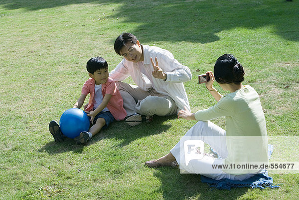 Family sitting on grass  woman taking photo of husband and son