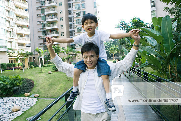 Boy riding on father's shoulders  front view  smiling at camera