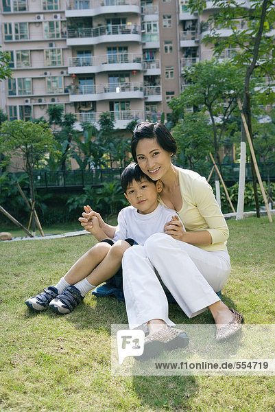 Mutter und Sohn sitzen auf Rasen vor dem Wohnhaus  volle Länge