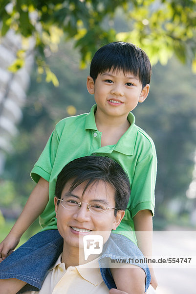 Boy sitting on father's shoulders  smiling at camera
