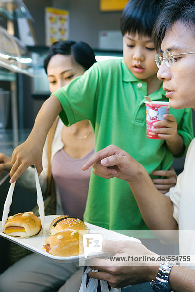 Familie isst Fast Food  Junge holt Brötchen vom Tablett.