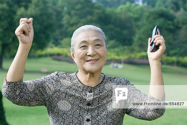 Ältere Frau  die Arme hebt  Handy hält