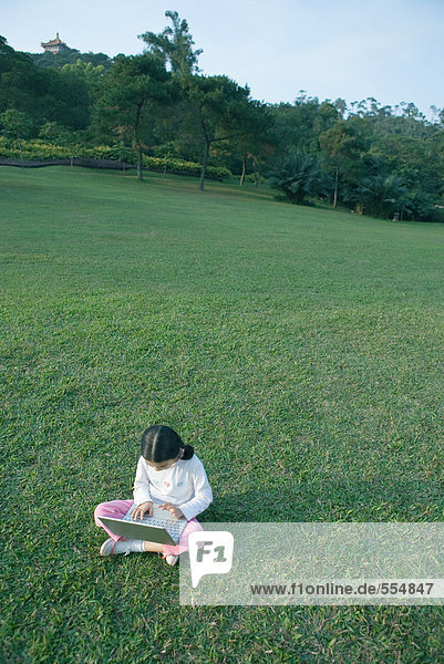 Mädchen im Gras sitzend mit Laptop