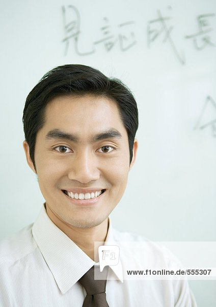 Businessman smiling  Chinese script on whiteboard in background  portrait