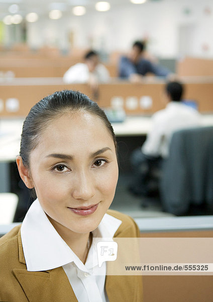 Geschäftsfrau lächelt vor der Kamera  Großraumbüro im Hintergrund