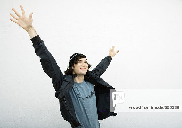 Junger Mann steht mit erhobenen Händen in der Luft.