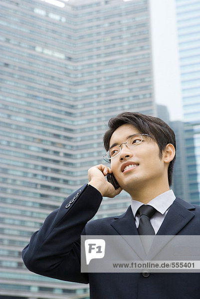 Junger Geschäftsmann mit dem Handy  wegschauen  Bürogebäude im Hintergrund