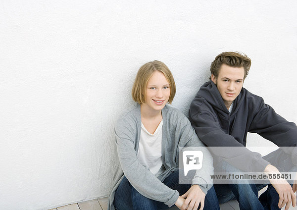 Young man and woman sitting on ground  leaning against wall