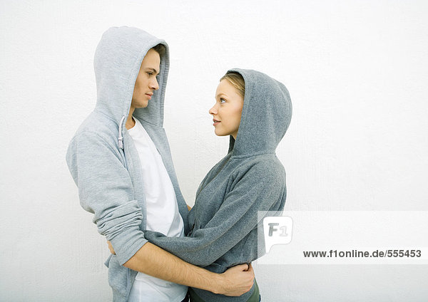 Young couple wearing hooded sweatshirts  holding each other around waist  face to face