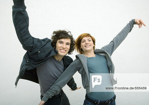 Junger Mann und junge Frau tanzen mit ausgestreckten Armen und lächeln in die Kamera.