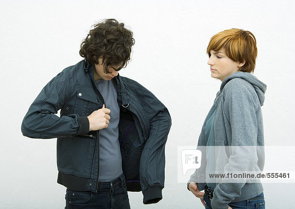 Young man and woman standing  man putting on jacket while woman watches