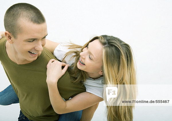 Young couple  man holding young woman on back  looking over shoulder  smiling at each other