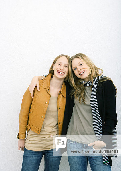 Zwei junge Freundinnen  eine mit Arm um die Schultern der anderen  beide lächelnd vor der Kamera