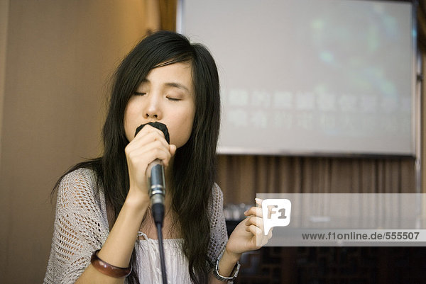 Junge Frau singt Karaoke  Augen zu.
