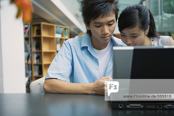 Young couple using laptop in library