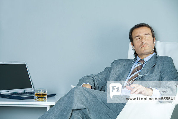 Businessman sitting listening to earphones with eyes closed
