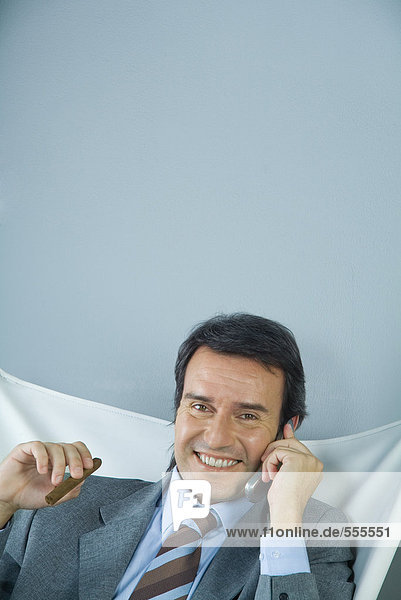 Businessman using cell phone and holding cigar  smiling at camera