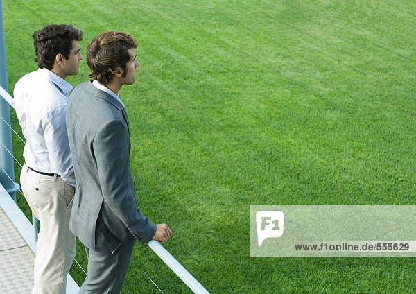 Two businessmen standing on walkway  looking into distance
