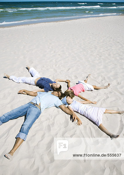 Familie auf Sand liegend  Köpfe zusammen und Arme und Beine ausgestreckt