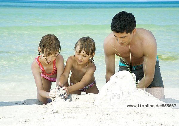 Vater und zwei Kinder spielen im Sand am Strand