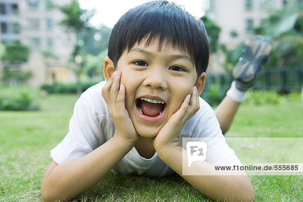 Boy lying on grass  holding head in hands  mouth wide open