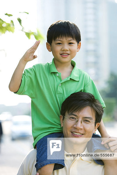 Man carrying son on shoulders  boy making gesture