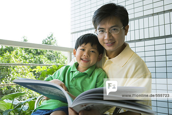 Vater und Sohn lesen Buch  lächeln vor der Kamera