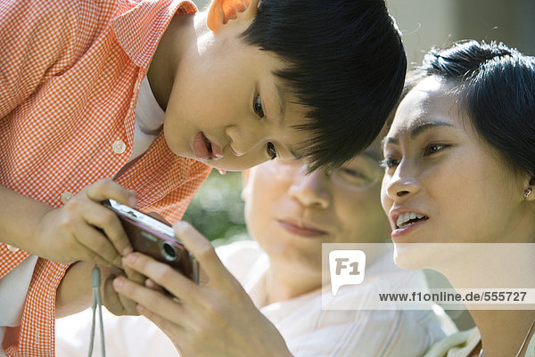 Junge mit Eltern  Mutter mit Digitalkamera  Junge bückt sich zum Anschauen
