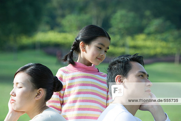 Mädchen schaut Eltern an  die Rücken an Rücken sitzen.
