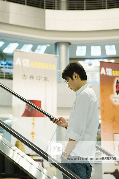 Man on escalator checking cell phone