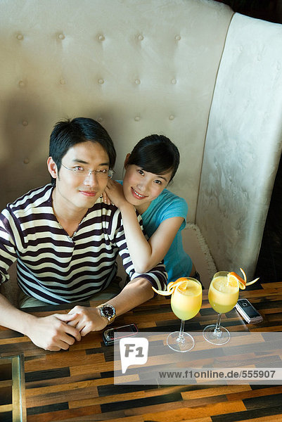 Couple sitting at booth with drinks on table  smiling at camera