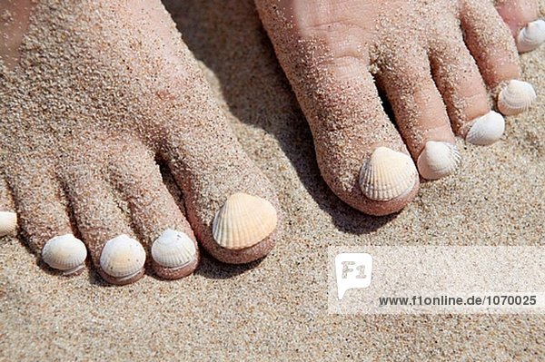 Seashells auf Woman´s Footnails auf sandigen Strand