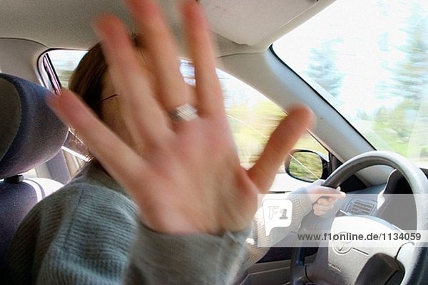 Junge Frau  mit Brille  ihr Auto fahren und Herauslehnen der Handfläche von ihrer Hand.