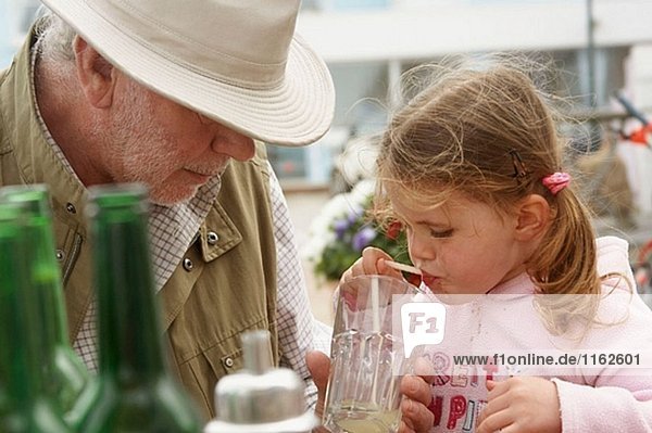 Grandad helfen seine 3 Jahre alten Enkelin mit ihr in einem externen Café trinken