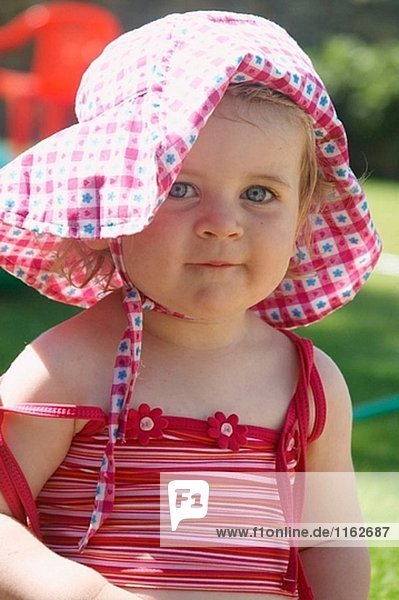18 Monate altes Mädchen sitzen außerhalb trägt einen großen floppy Hut  lächelnd in Kamera
