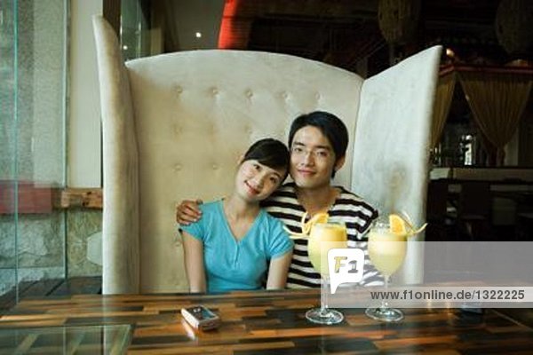 Young couple sitting in booth  cocktails on table  smiling at camera