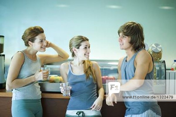 Young adults wearing exercise clothes  standing in cafeteria  having healthy snack and chatting