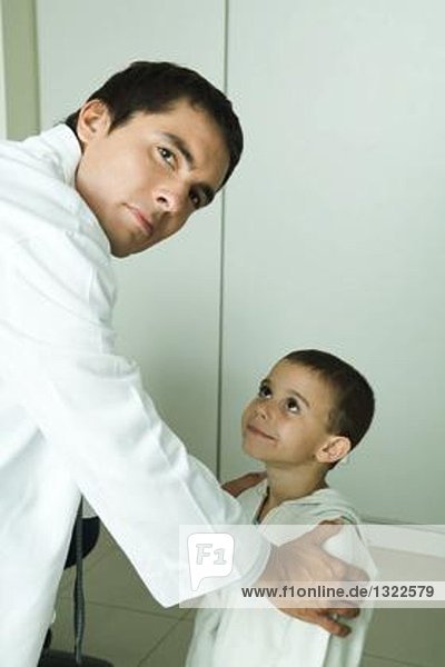 Boy looking up at doctor  doctor holding boy by shoulders  looking over shoulder at camera