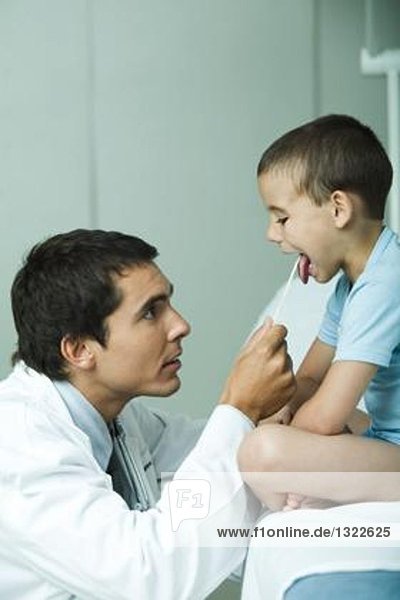 Arzt hält die Zunge des Jungen mit Zungenspatel fest
